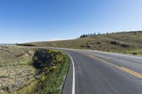 a yellow road next to the hills and fields, on a clear day with blue skies