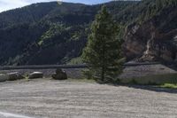 two motorcycles are stopped near the water and mountains in the background with trees, rocks, gravel path and riverbank