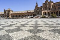 a crowd is walking around in the courtyard of an ornate building with circular patterns on stone flooring