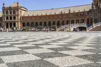 a crowd is walking around in the courtyard of an ornate building with circular patterns on stone flooring