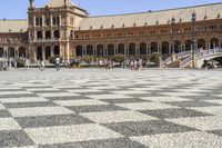 a crowd is walking around in the courtyard of an ornate building with circular patterns on stone flooring