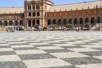 a crowd is walking around in the courtyard of an ornate building with circular patterns on stone flooring