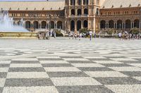 a crowd is walking around in the courtyard of an ornate building with circular patterns on stone flooring