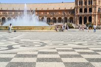 a crowd is walking around in the courtyard of an ornate building with circular patterns on stone flooring