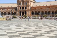 a crowd is walking around in the courtyard of an ornate building with circular patterns on stone flooring