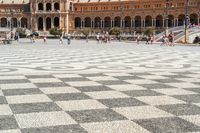 a crowd is walking around in the courtyard of an ornate building with circular patterns on stone flooring