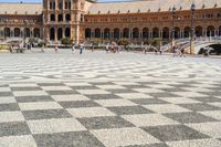 a crowd is walking around in the courtyard of an ornate building with circular patterns on stone flooring