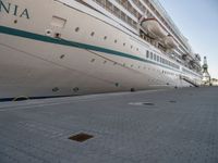 the cruise ship is docked behind a chain link fenced walkway on brick ground next to another boat