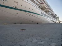 the cruise ship is docked behind a chain link fenced walkway on brick ground next to another boat