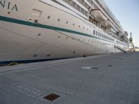 the cruise ship is docked behind a chain link fenced walkway on brick ground next to another boat