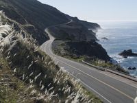 the curve of a beach road stretches from cliffs above the water to land below it