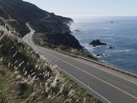 the curve of a beach road stretches from cliffs above the water to land below it