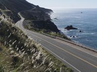 the curve of a beach road stretches from cliffs above the water to land below it