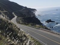 the curve of a beach road stretches from cliffs above the water to land below it