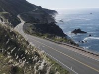 the curve of a beach road stretches from cliffs above the water to land below it