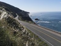 the curve of a beach road stretches from cliffs above the water to land below it