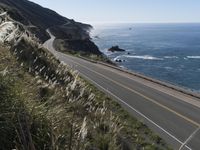 the curve of a beach road stretches from cliffs above the water to land below it