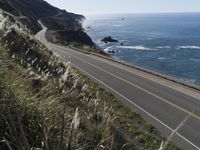 the curve of a beach road stretches from cliffs above the water to land below it