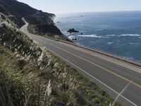 the curve of a beach road stretches from cliffs above the water to land below it