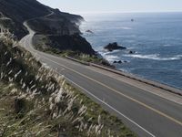 the curve of a beach road stretches from cliffs above the water to land below it