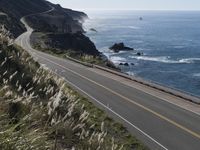 the curve of a beach road stretches from cliffs above the water to land below it