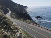 the curve of a beach road stretches from cliffs above the water to land below it