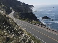 the curve of a beach road stretches from cliffs above the water to land below it