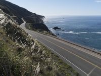 the curve of a beach road stretches from cliffs above the water to land below it