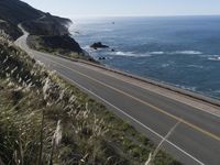 the curve of a beach road stretches from cliffs above the water to land below it