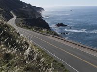 the curve of a beach road stretches from cliffs above the water to land below it