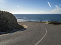 there is a curved curve near the ocean, road or highway with sea view and blue sky