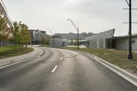 a curve road with buildings in the back ground and green grass on either side and street light pole in front