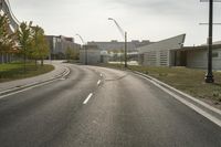 a curve road with buildings in the back ground and green grass on either side and street light pole in front