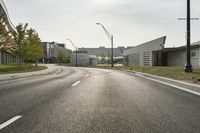 a curve road with buildings in the back ground and green grass on either side and street light pole in front