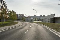 a curve road with buildings in the back ground and green grass on either side and street light pole in front