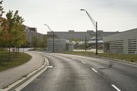 a curve road with buildings in the back ground and green grass on either side and street light pole in front