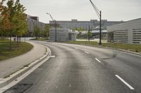 a curve road with buildings in the back ground and green grass on either side and street light pole in front