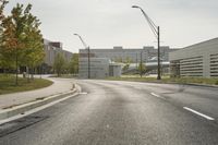 a curve road with buildings in the back ground and green grass on either side and street light pole in front