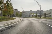 a curve road with buildings in the back ground and green grass on either side and street light pole in front