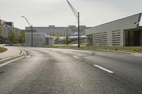 a curve road with buildings in the back ground and green grass on either side and street light pole in front