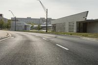 a curve road with buildings in the back ground and green grass on either side and street light pole in front