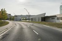 a curve road with buildings in the back ground and green grass on either side and street light pole in front