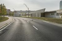 a curve road with buildings in the back ground and green grass on either side and street light pole in front