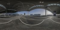 a large curved airport terminal with cars on the road and some buildings in the distance