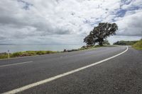 a lone motorcyclist on a curved road near the ocean and sky with clouds