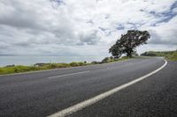 a lone motorcyclist on a curved road near the ocean and sky with clouds