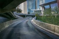 a curved asphalt road under a bridge in the city during sunset time with a low glow