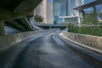 a curved asphalt road under a bridge in the city during sunset time with a low glow