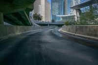 a curved asphalt road under a bridge in the city during sunset time with a low glow