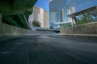 a curved asphalt road under a bridge in the city during sunset time with a low glow